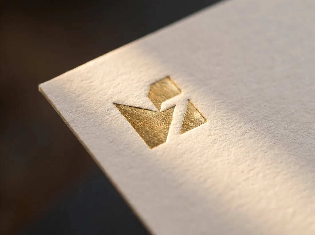 Gold foil mark pressed into textured cream card stock, lit to show the metallic shine